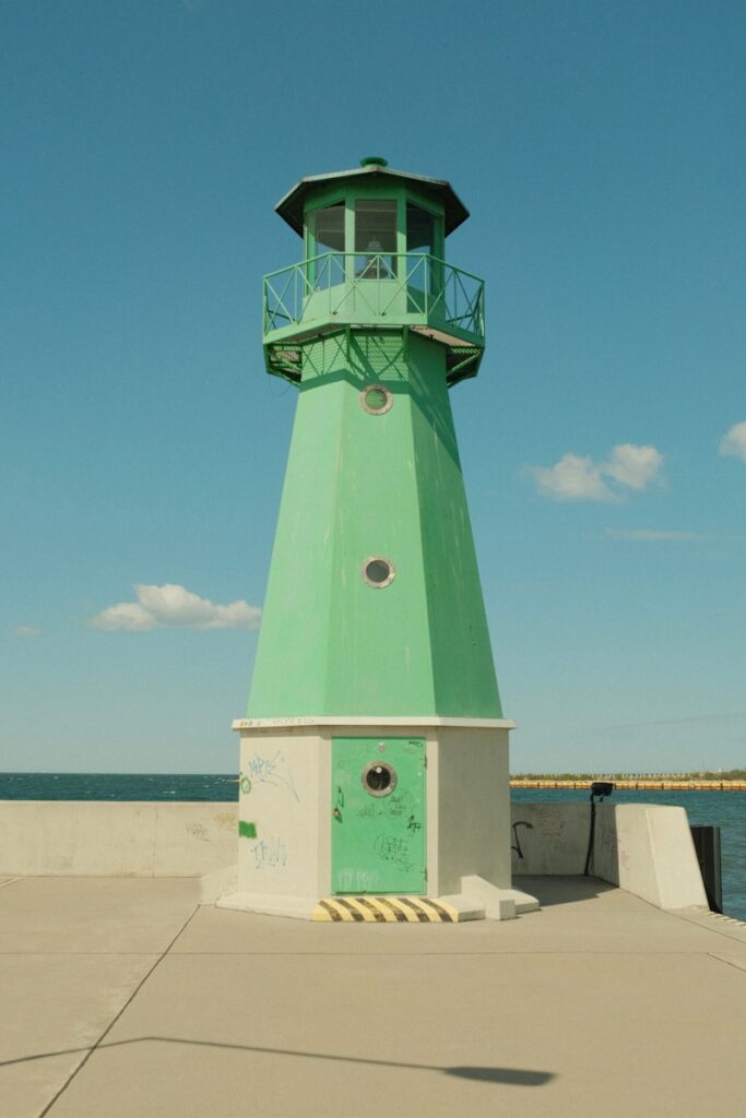 A green lighthouse stands tall against a blue sky.
