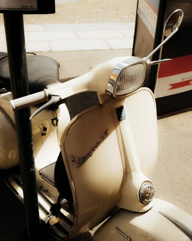 A classic cream-colored vespa scooter is parked.